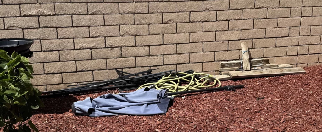 Backyard debris with hose and tarp staged for junk removal