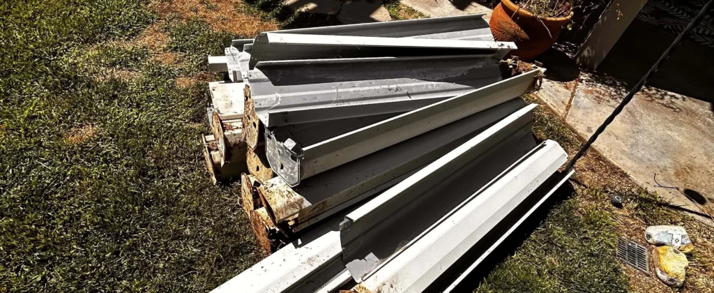 Discarded rain gutters stacked on residential lawn for removal